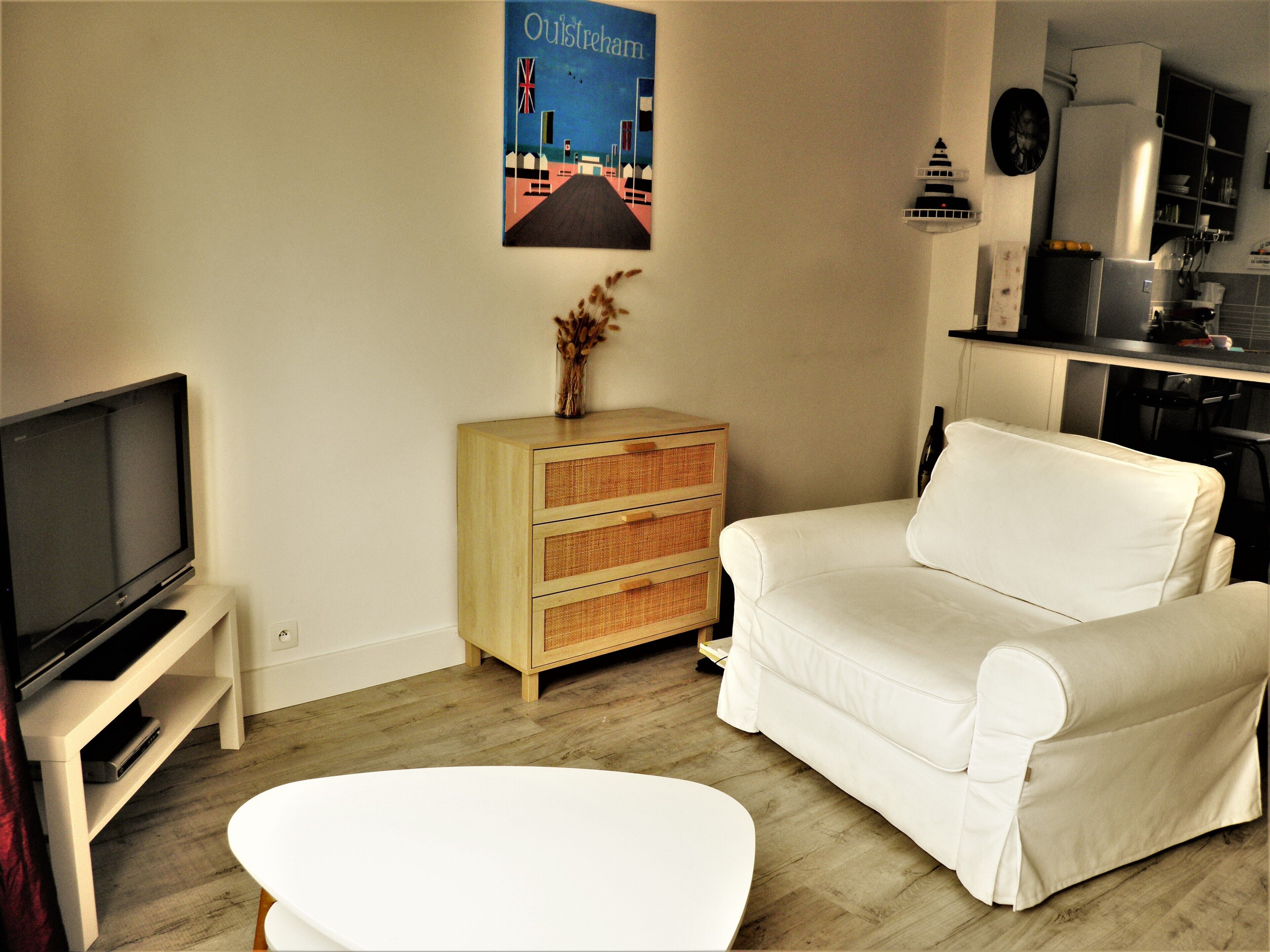 A living room with a television, a white sofa, a wooden cabinet, and a poster on the wall.