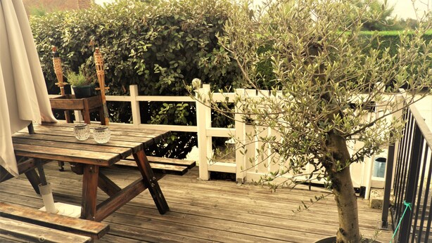 A wooden deck with a table and chairs, surrounded by a white fence and a potted tree.