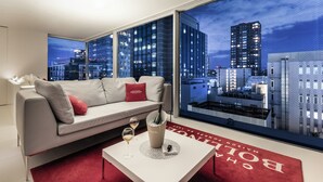 A modern living room with a sofa, a table with a bottle and glass, and a large window with a city view. - CUVEE J2 HOTEL OSAKA by Onko Chishin (Osaka)