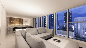 A modern living room with a sofa, a coffee table, and a dining area with a table and chairs. Large windows offer a view of the cityscape at night. - CUVEE J2 HOTEL OSAKA by Onko Chishin (Osaka)