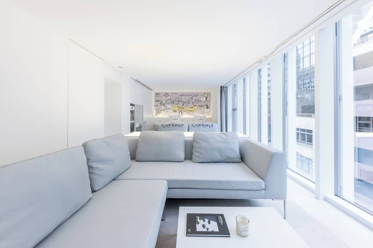 A modern, minimalist living room with a large window, a sofa, a coffee table, and a wall-mounted artwork.