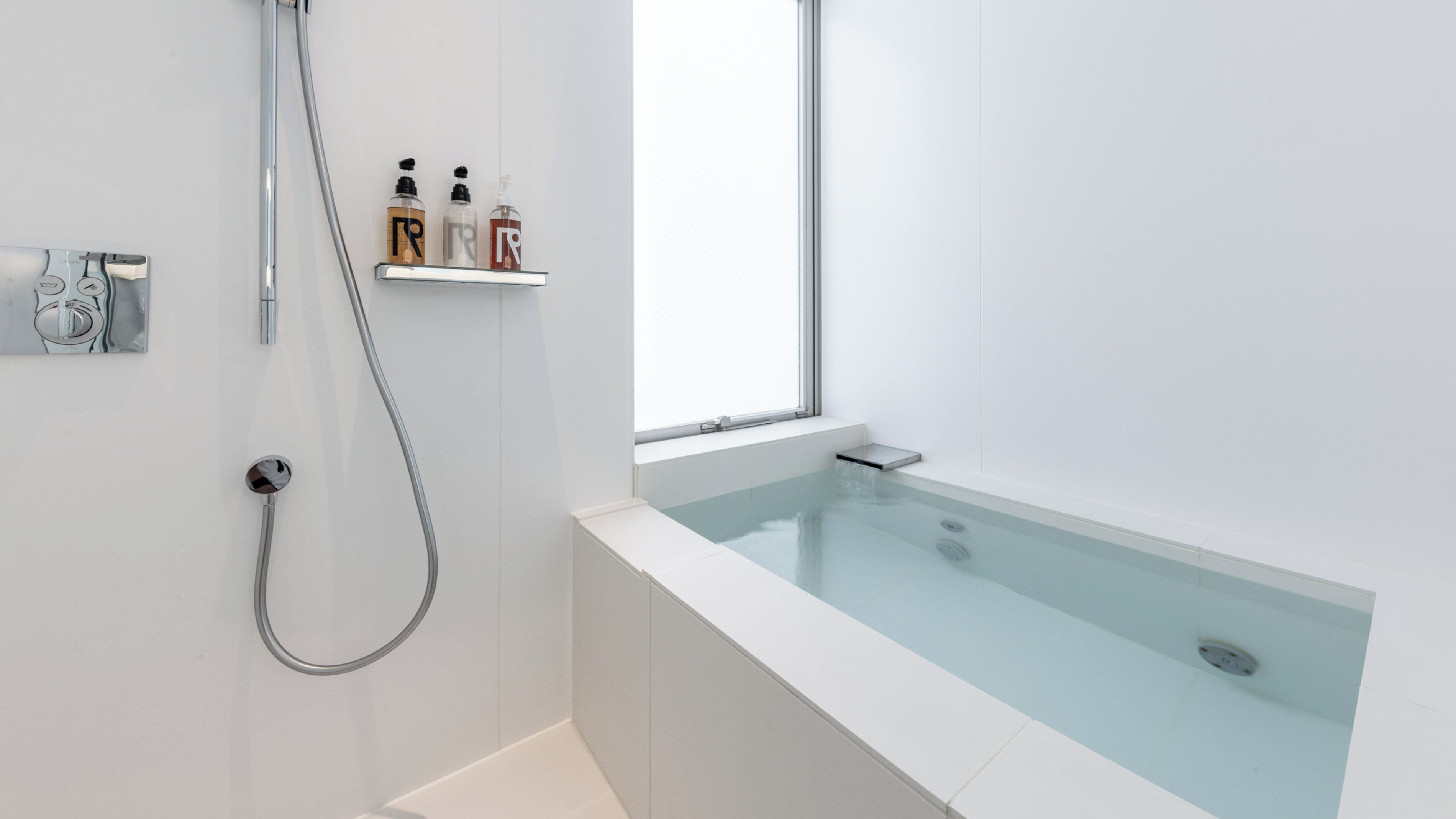 Een moderne badkamer met een glazen badkuip, een douchekop en een raam.