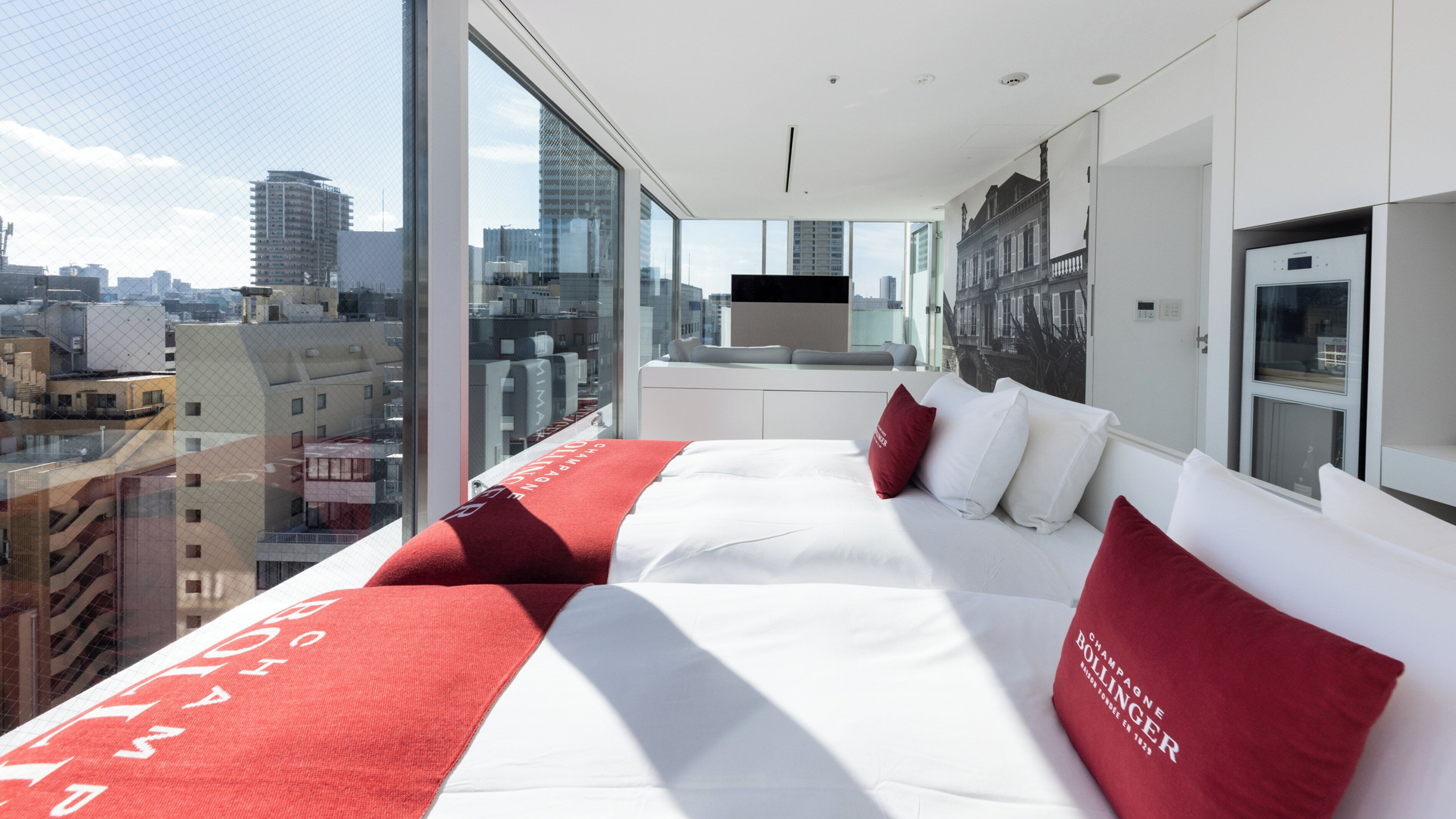 A modern hotel room with a large bed, a city view, and a kitchenette.