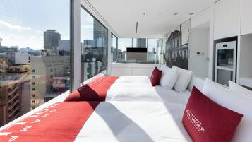 A modern hotel room with a large bed, a city view, and a kitchenette.