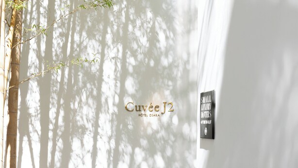 A sign for Cuvee J2 Hotel Osaka with a bamboo tree and a sign for Small Luxury Hotels.