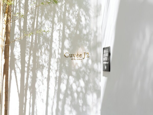 Señal del Hotel Cuvee J2 Osaka con un árbol de bambú y una señal de Small Luxury Hotels.