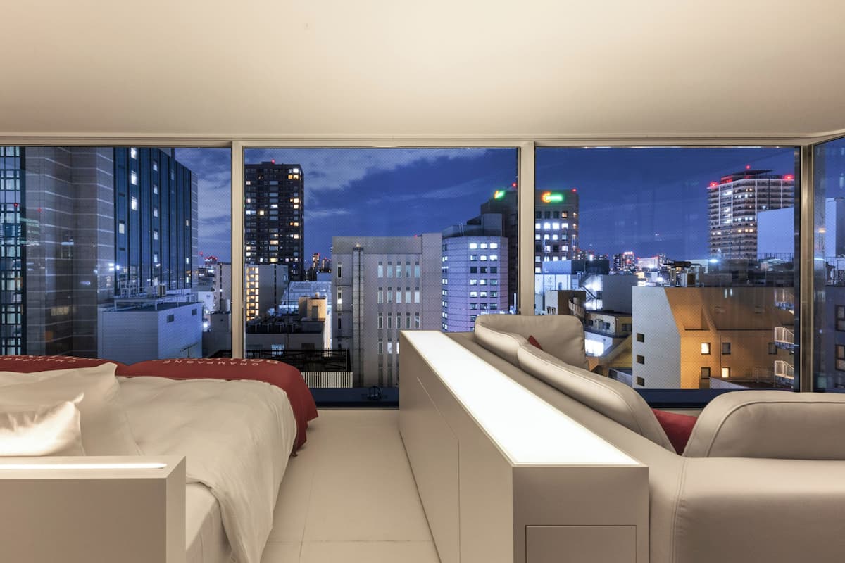 A modern hotel room with a large window offering a city view at night.