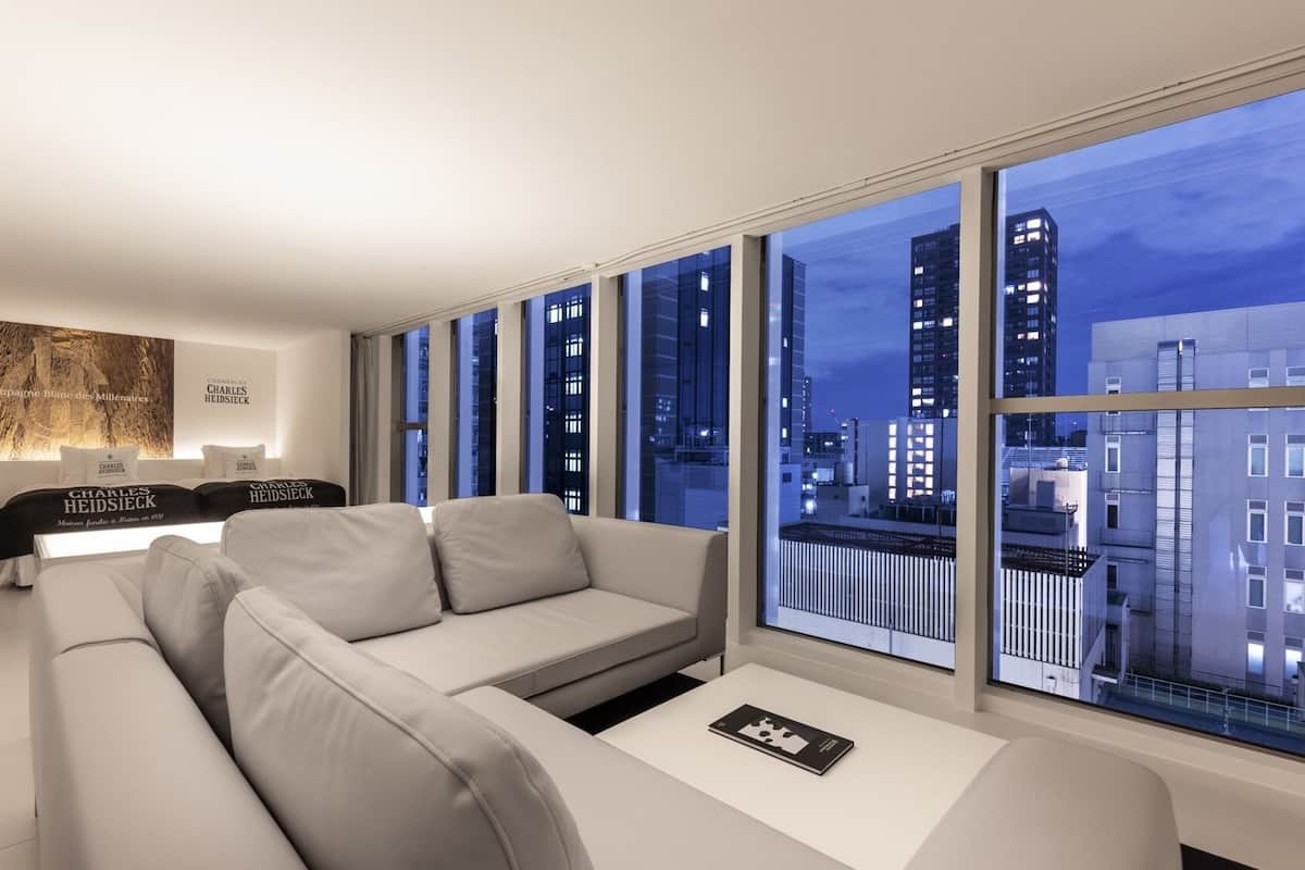 A modern living room with a sofa, a coffee table, and a view of the cityscape through large windows.
