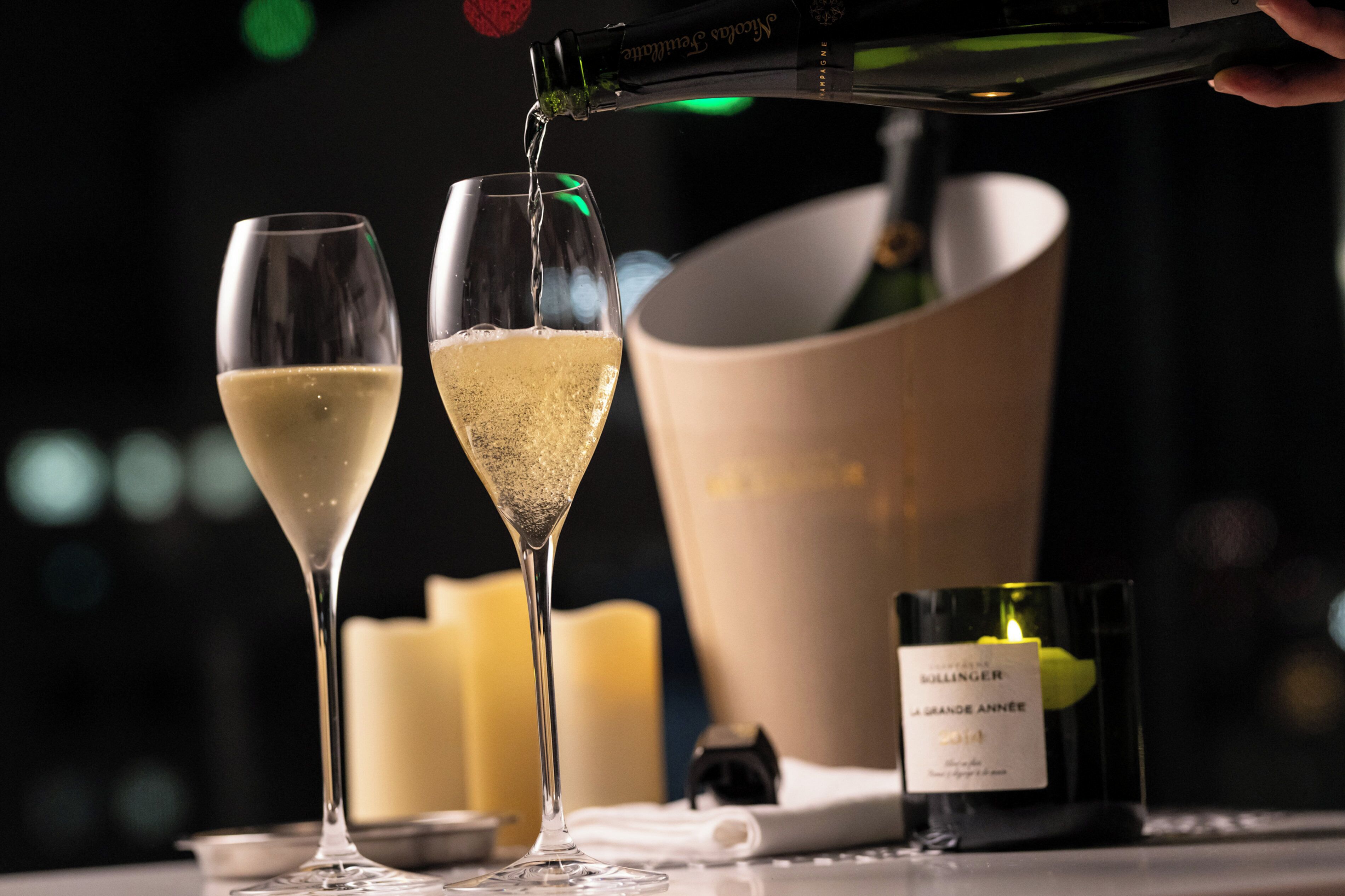 Twee champagneglazen gevuld met champagne, een champagnefles en een kaars op een tafel.