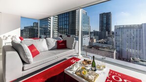 A modern hotel room with a grey sofa, red cushions, a dining table with breakfast items, and a city view through large windows. - CUVEE J2 HOTEL OSAKA by Onko Chishin (Osaka)