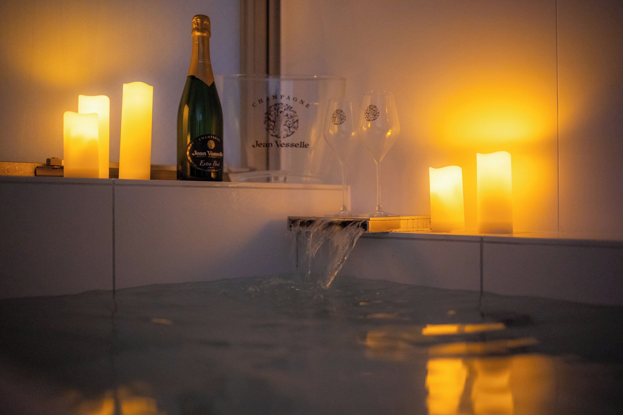 A bar area with candles, a bottle of champagne, and glasses on a shelf.
