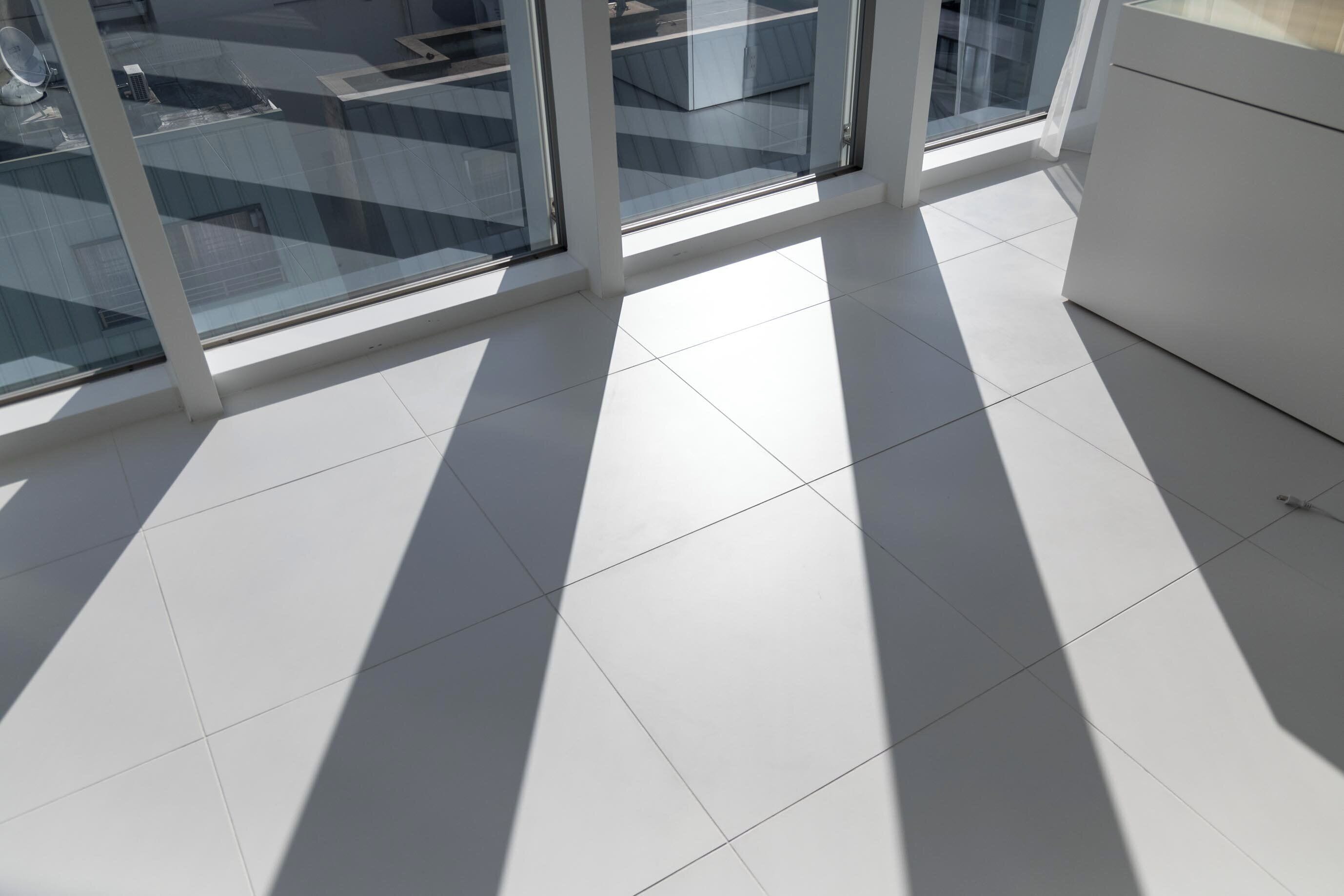 A modern room with large windows, white tiled flooring, and a white cabinet.