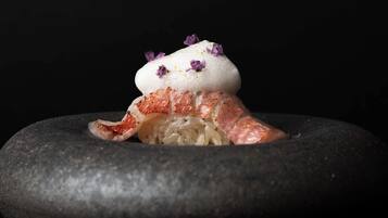Un piatto con un'alta porzione di riso, condito con una crema e guarnito con fiori viola, servito su un piatto di pietra scura.
