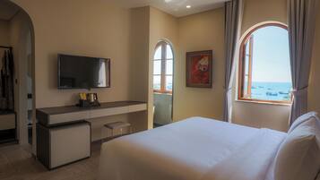 Een hotelkamer met een bed, een bureau, een televisie, een kleine koelkast en een raam met uitzicht op zee.