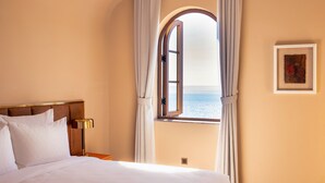 Habitación de hotel con una cama grande, una mesita de noche, una lámpara, un cuadro enmarcado y una ventana con cortinas.