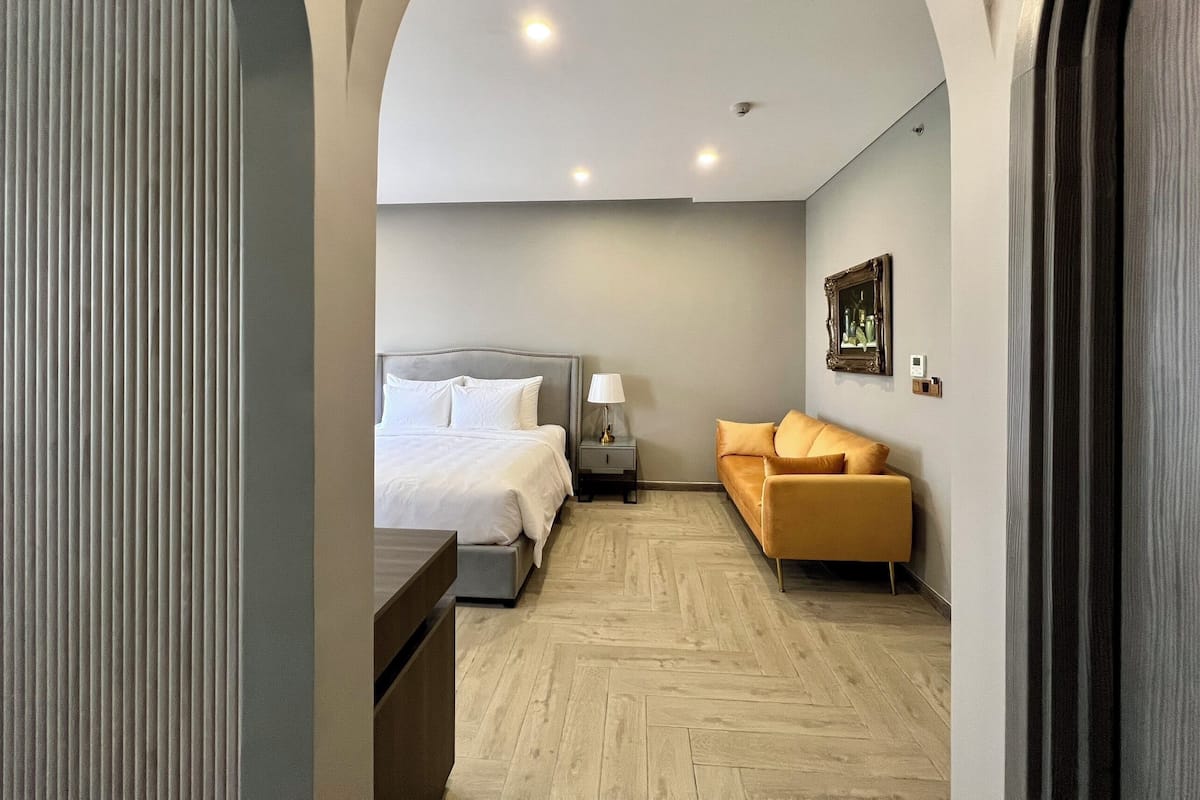 A modern hotel room with a bed, a sofa, a nightstand, and a painting on the wall.