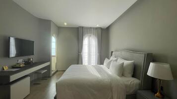 A modern hotel room with a large bed, a bedside table with a lamp, a TV mounted on the wall, and a desk with a chair.
