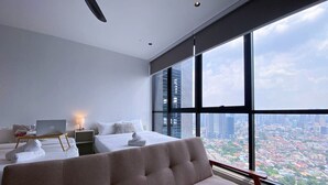 A modern hotel room with a large bed, a desk with a laptop, a sofa, and a view of a cityscape through large windows. - High Floor KL View Scarletz Suite (Kuala Lumpur)