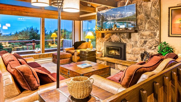 A cozy living room with a stone fireplace, leather sofas, and a large window offering a mountain view. - Brathouse By The Sea (Copalis Beach)
