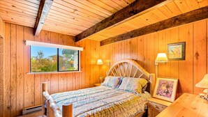 A wooden-paneled bedroom with a bed, bedside lamps, a window, and a table. - Brathouse By The Sea (Copalis Beach)