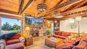 A cozy living room with a stone fireplace, red leather sofas, and wooden ceiling beams. - Brathouse By The Sea (Copalis Beach)
