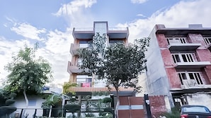 Um edifício residencial com várias andares, varandas, portão fechado e uma árvore à frente.