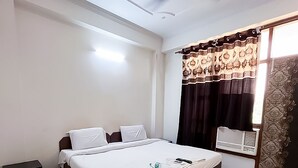 Quarto de hotel com cama, ventilador de teto, janela com cortinas e mesa de cabeceira.