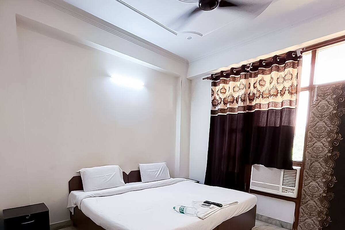 Una habitación de hotel con una cama, un ventilador de techo, una ventana con cortinas y una mesita de noche.