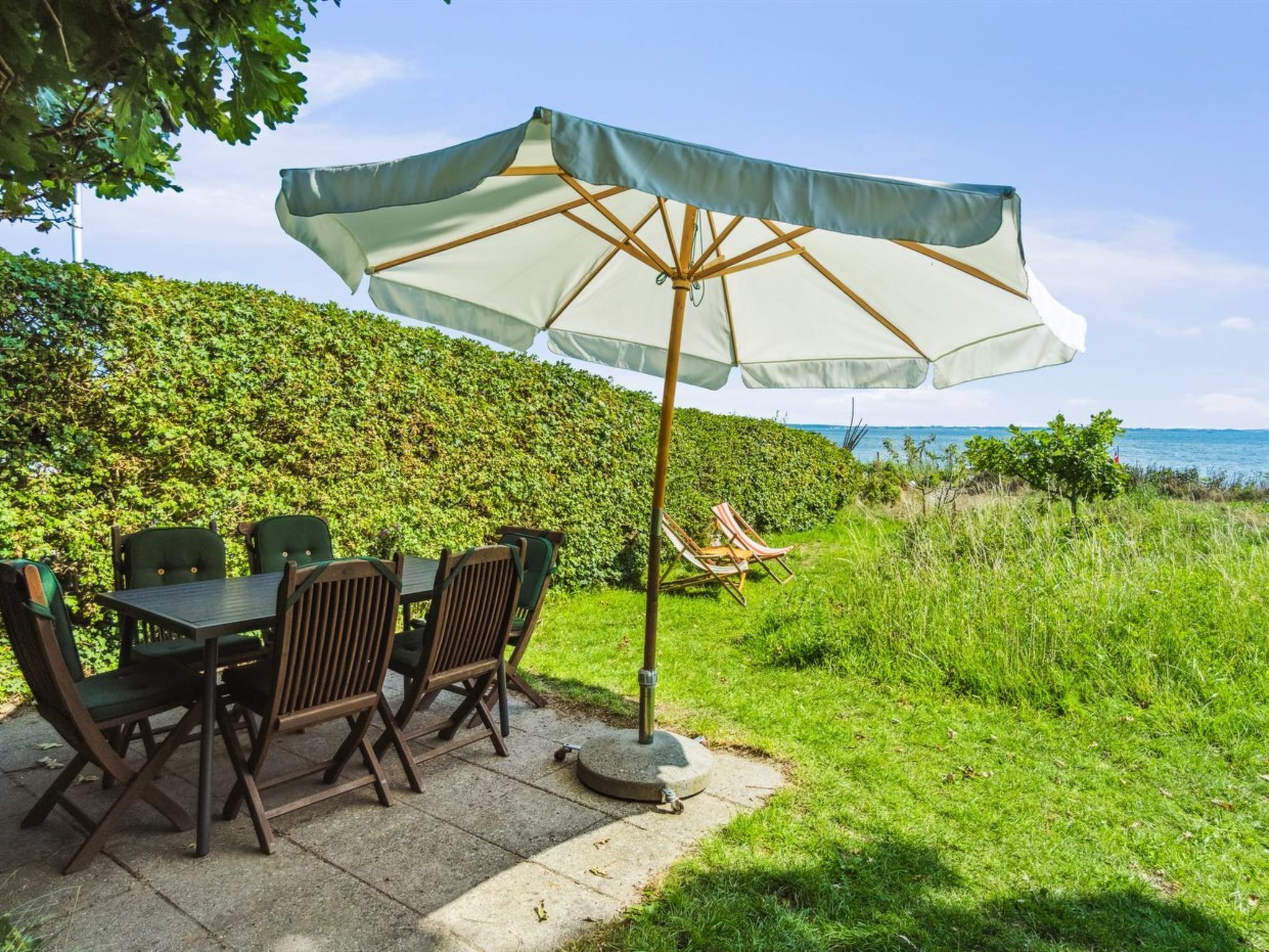 An outdoor patio with a table and chairs, a large umbrella, and a view of the sea.