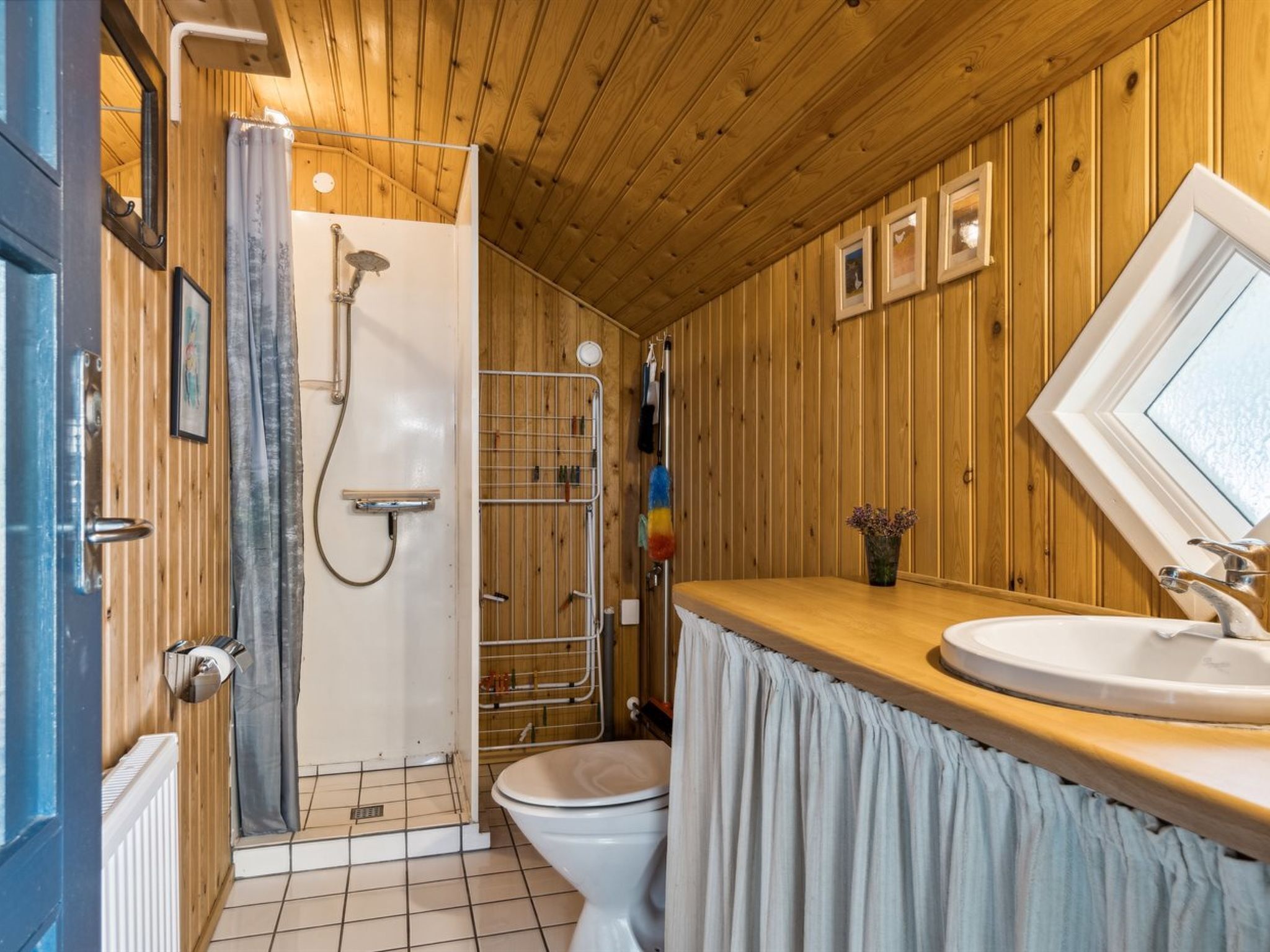 Une salle de bain aux murs lambrissés, équipée d’une douche, de toilettes et d’un lavabo.