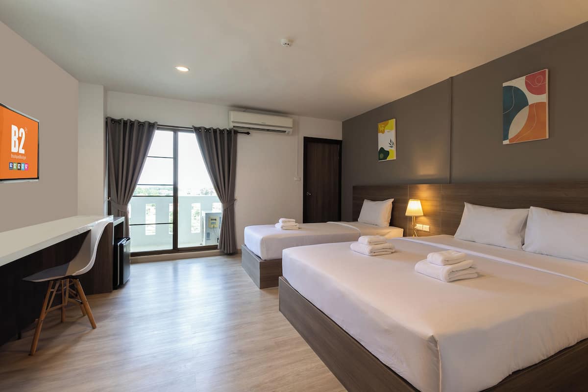 Une chambre d’hôtel avec deux lits, un bureau et une grande fenêtre avec des rideaux.