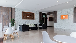 Un hall d’entrée moderne avec des murs en marbre, un comptoir d’accueil, un espace détente et un écran numérique.