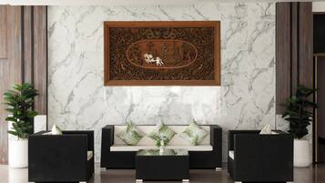 A lobby with a marble wall, a framed artwork, a sofa, and two potted plants.