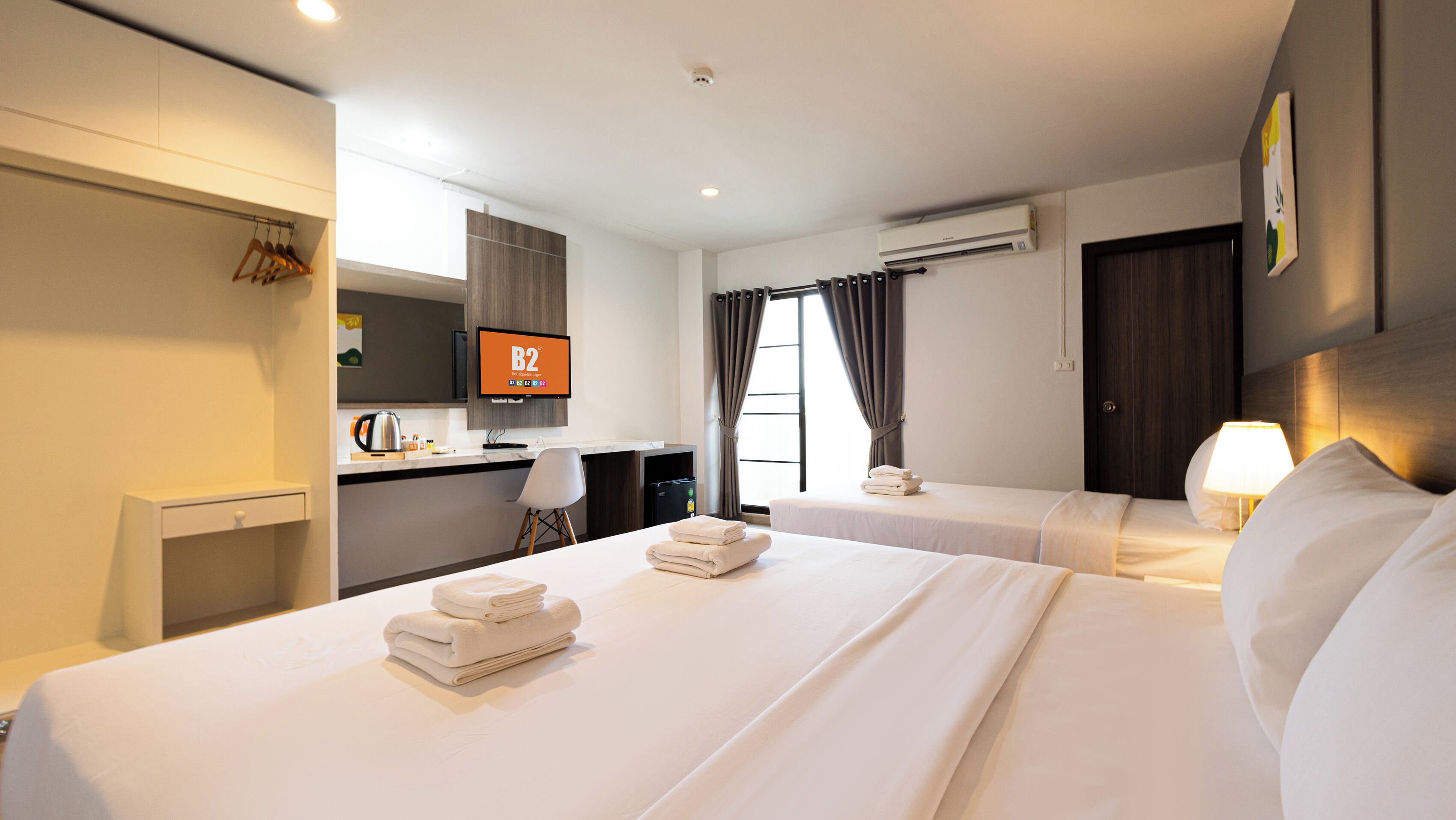 Une chambre d’hôtel avec deux lits, un bureau, une télévision, un appareil de climatisation et une fenêtre avec des rideaux.