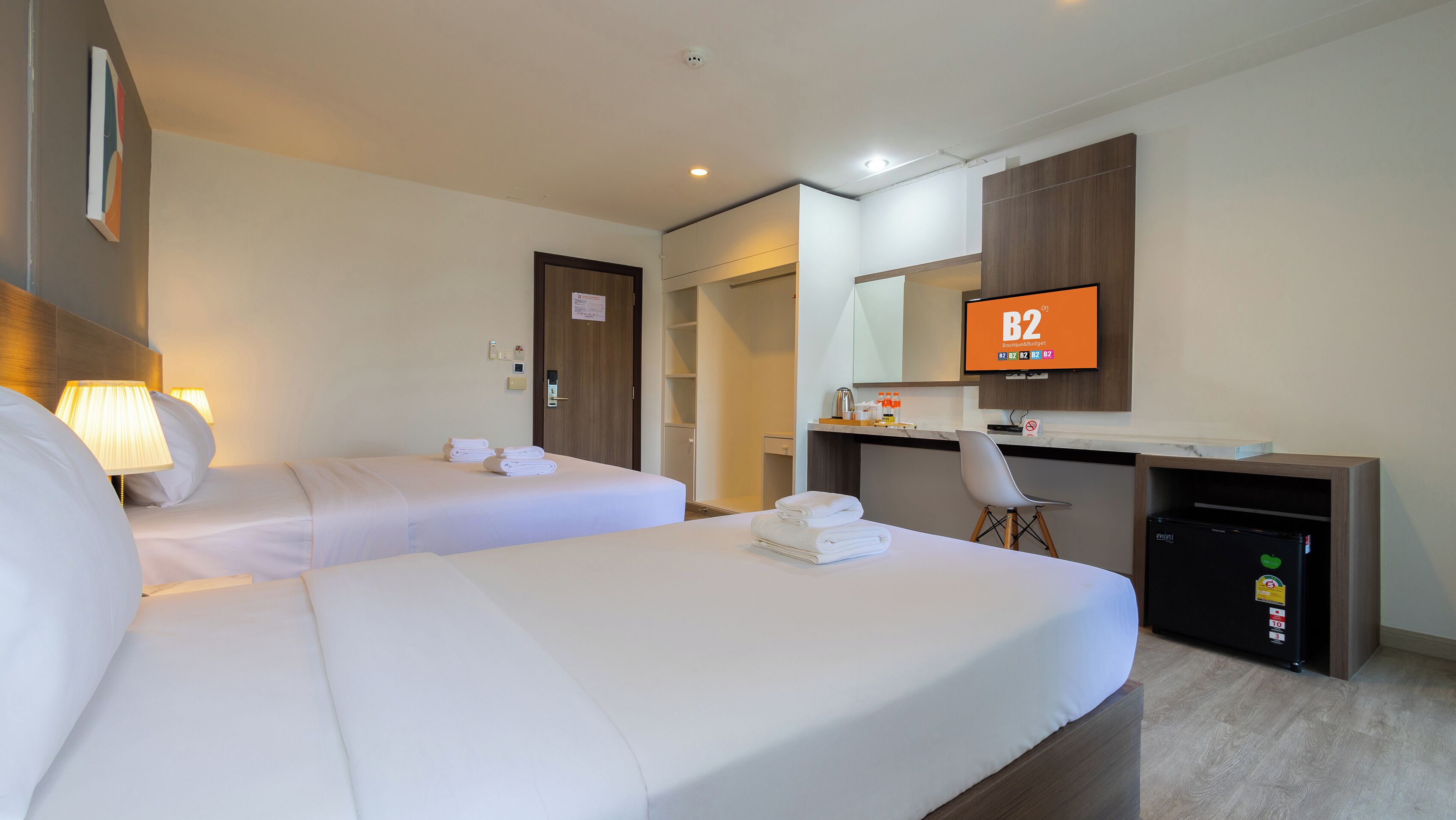 A hotel room with two beds, a desk, a chair, a TV, and a minibar.