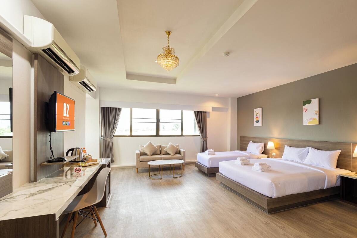 Une chambre d’hôtel avec deux lits, un bureau, une chaise, une télévision et un lustre.