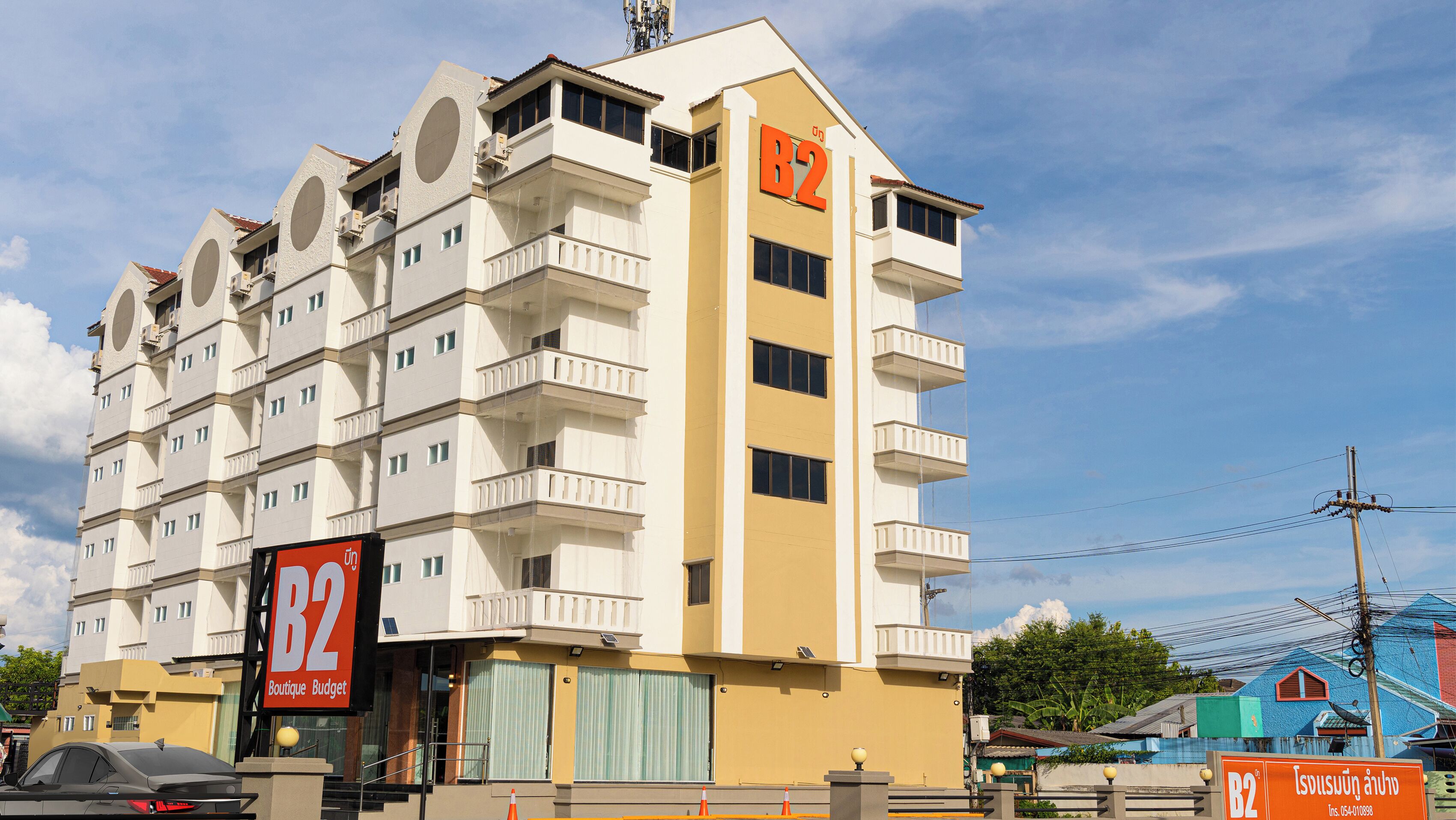 Um hotel com vários andares, varandas, um sinal chamativo com a letra 'B2' e um letreiro indicando 'Boutique Budget'.