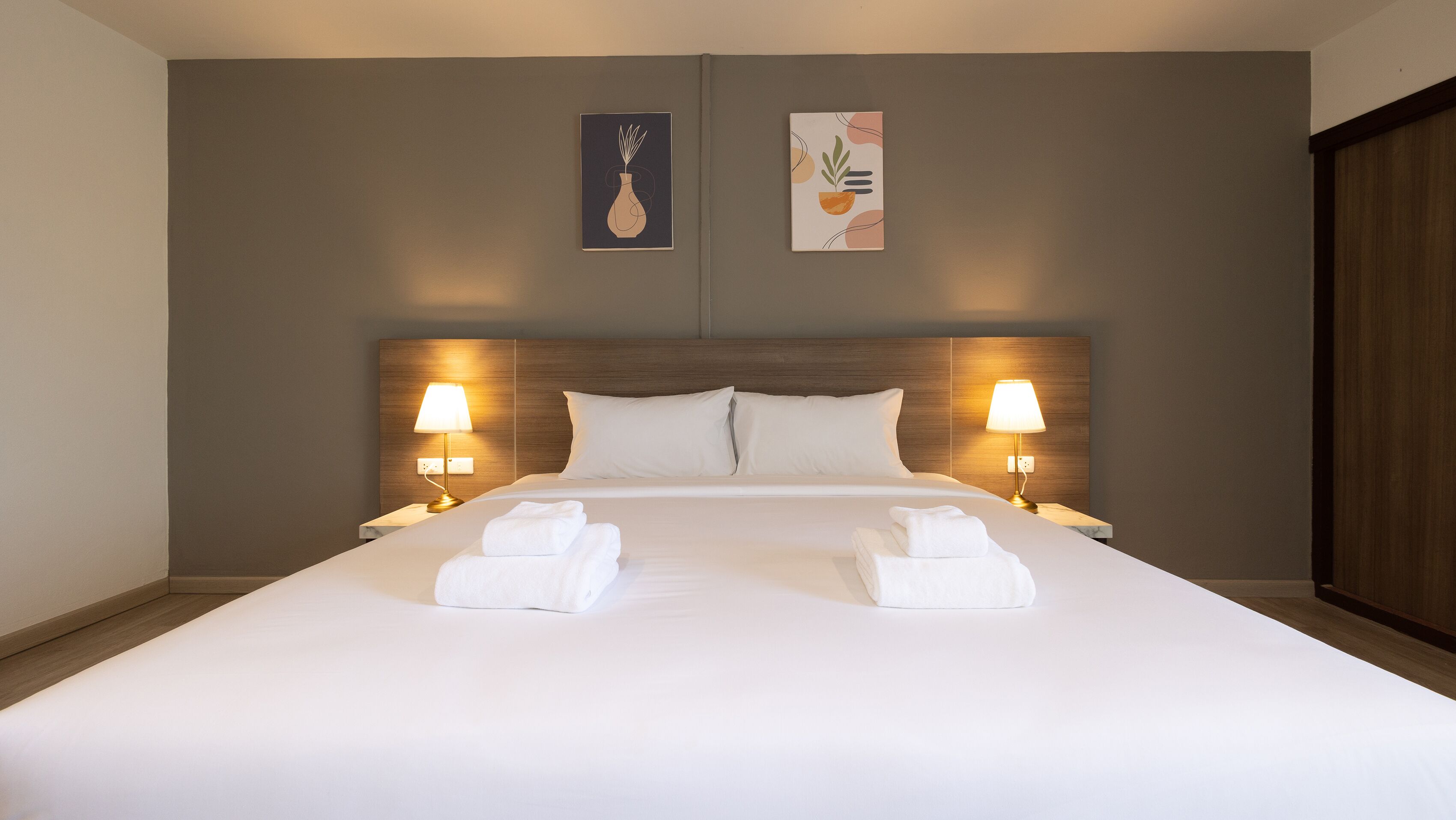 A neatly made bed with white linens and two towels, flanked by two bedside lamps.