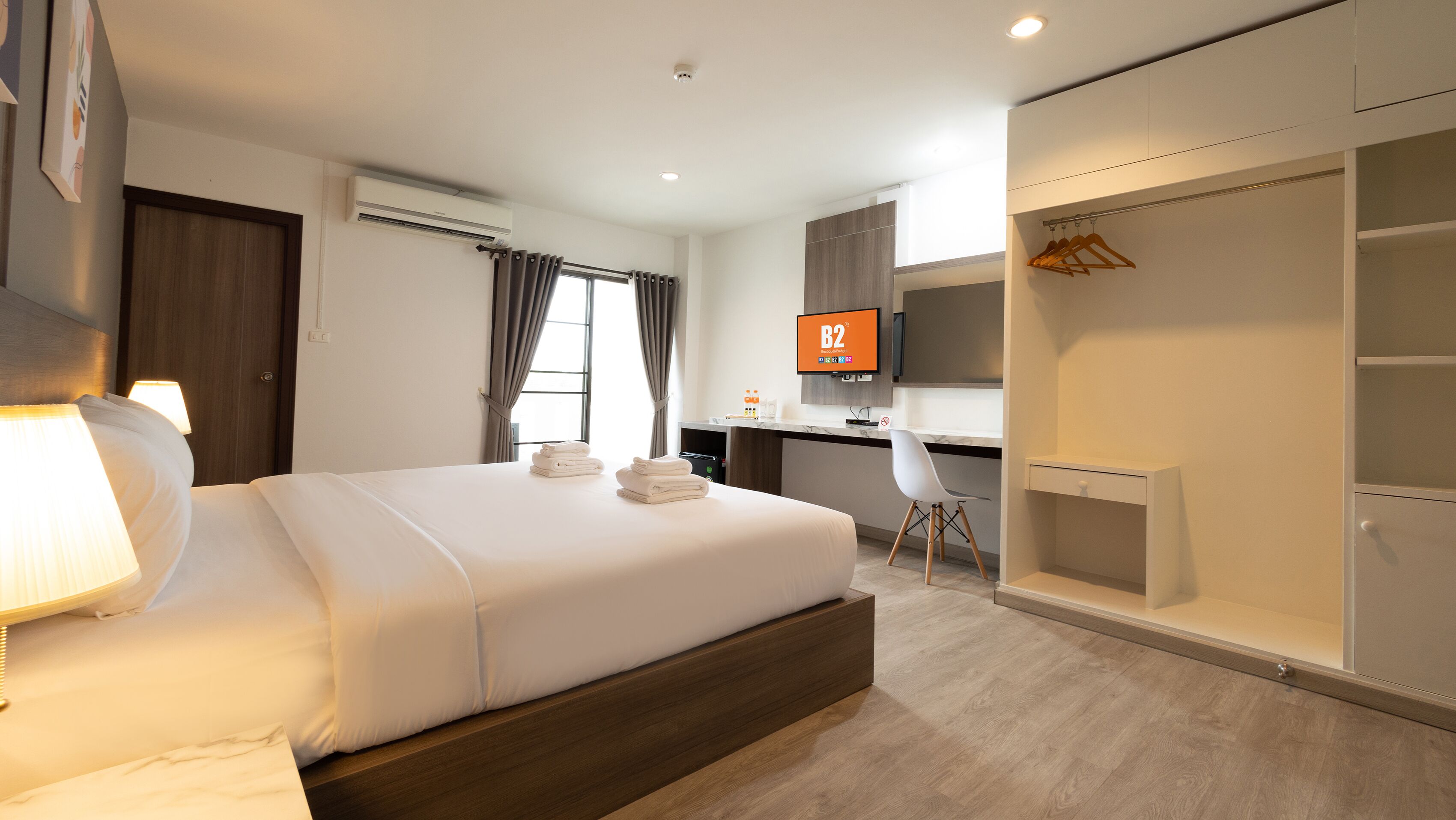 Une chambre d’hôtel moderne équipée d’un grand lit, d’un bureau, d’une armoire et d’un téléviseur affichant « B2 ».