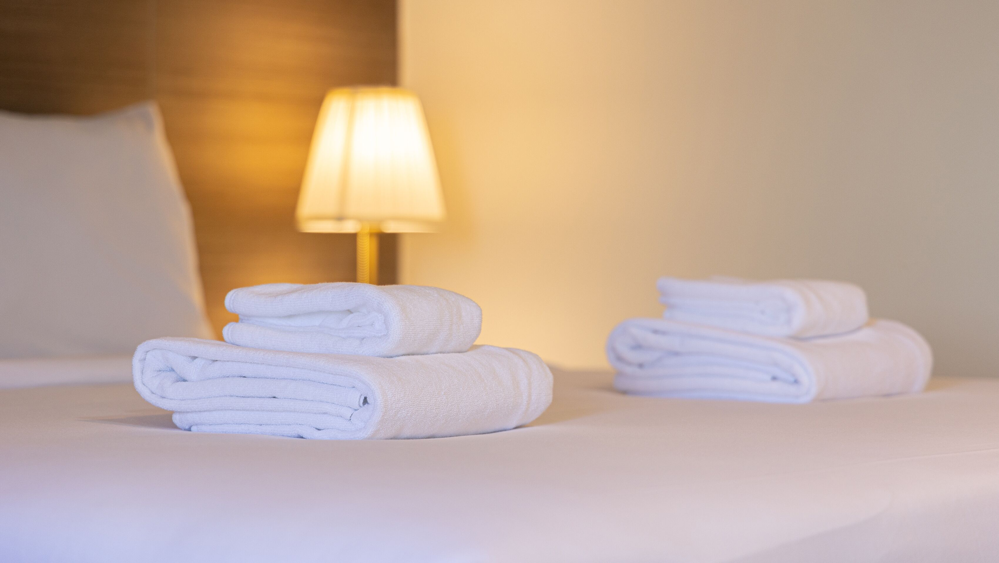 Una cama bien hecha con toallas blancas dobladas y una lámpara de noche.