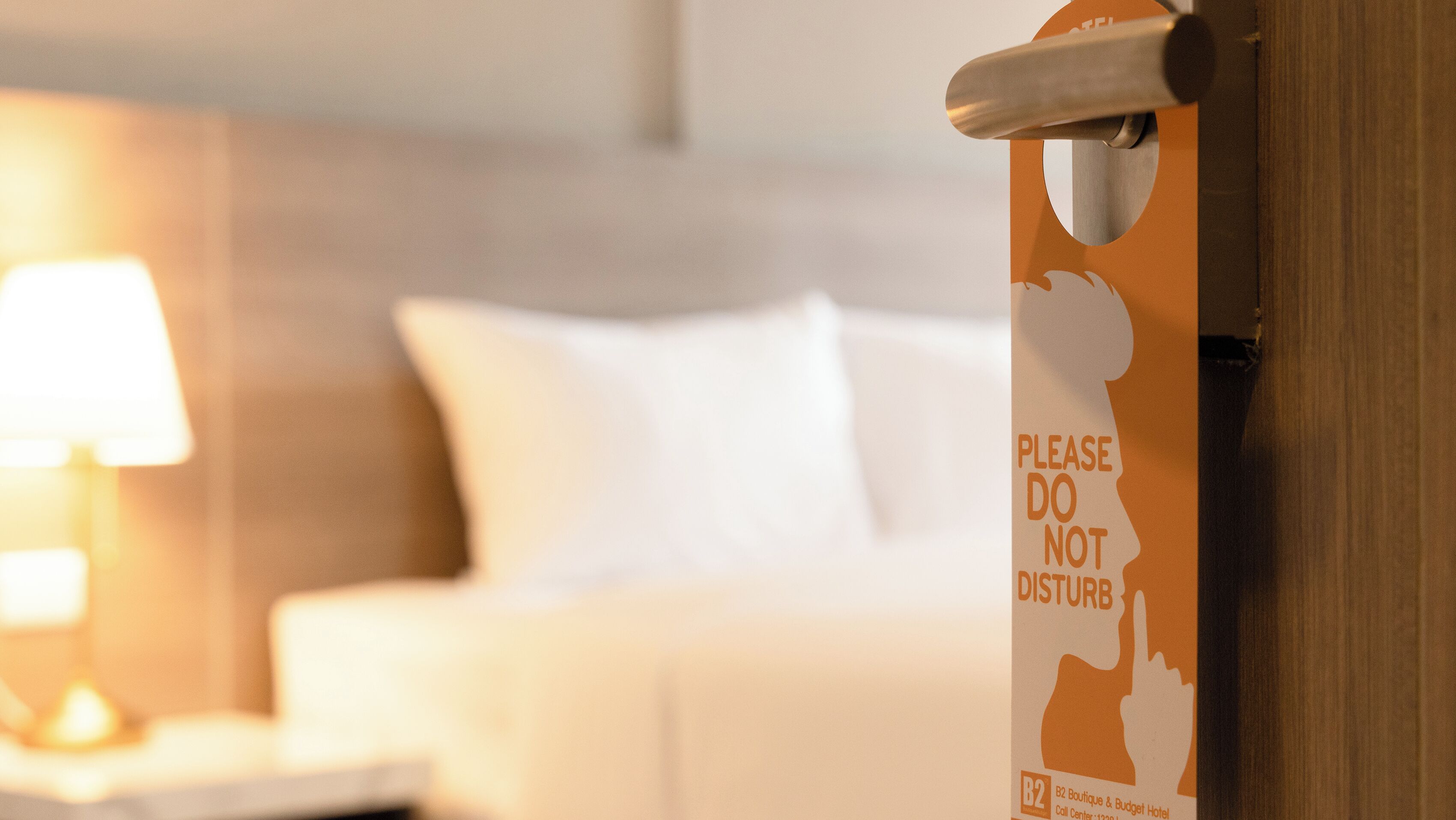 A hotel room with a bed, a nightstand, and a sign on the door that reads "PLEASE DO NOT DISTURB".