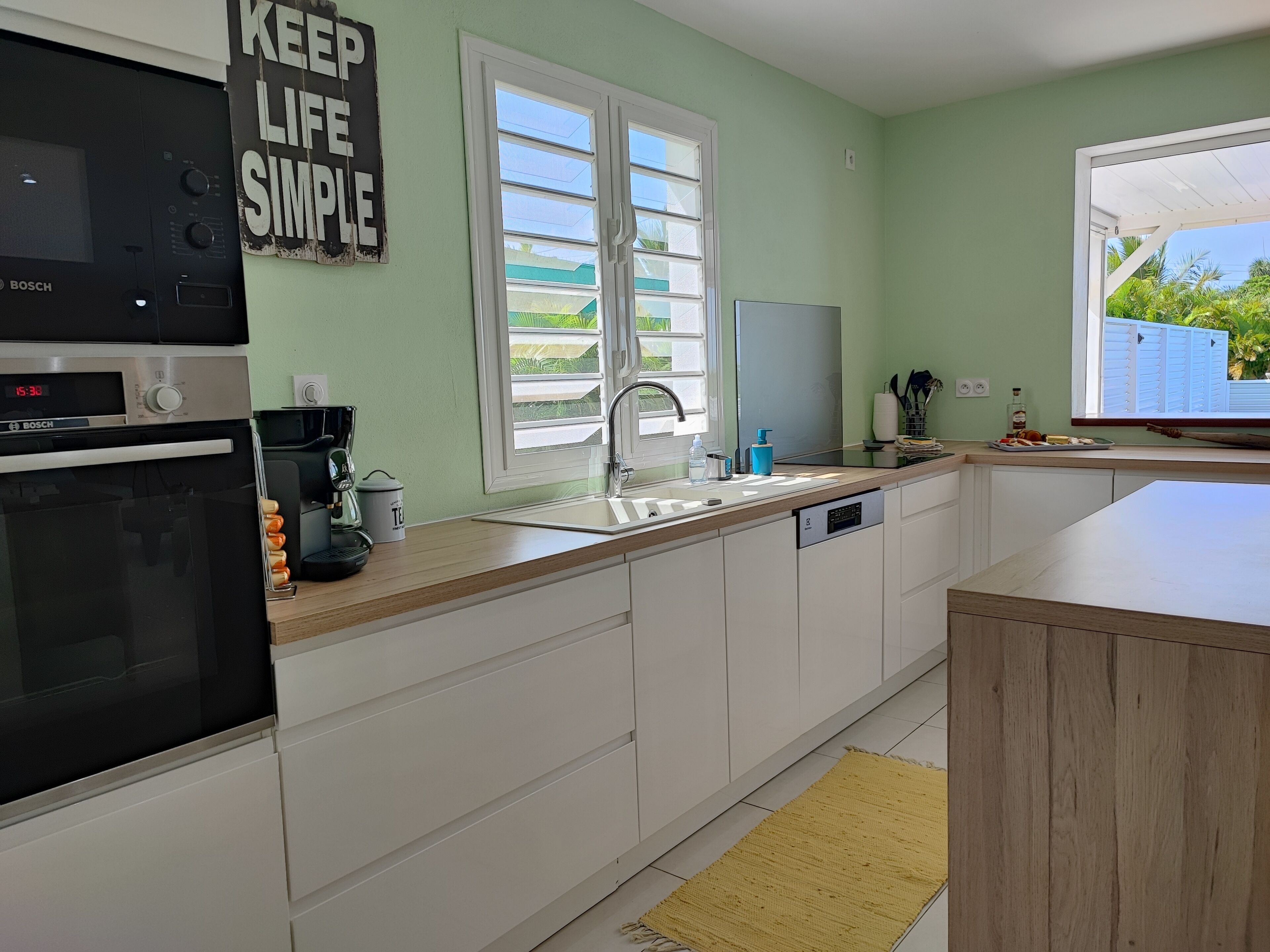 Eine moderne Küche mit weißen Schränken, einem Bosch-Ofen, einer Kaffeemaschine und einem Spülbecken mit Fenster darüber.