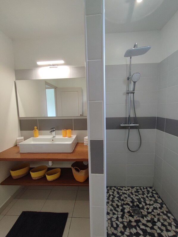 A bathroom with a white sink, mirror, and shower. There are yellow baskets under the sink and a black and white tiled floor. - Magnificent Villa "Ti Kaz An Nou" - private pool - 3 min from the beach (Sainte-Rose)