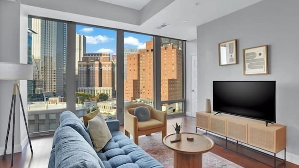 A modern living room with a large window, a sofa, a chair, a coffee table, and a flat-screen TV.