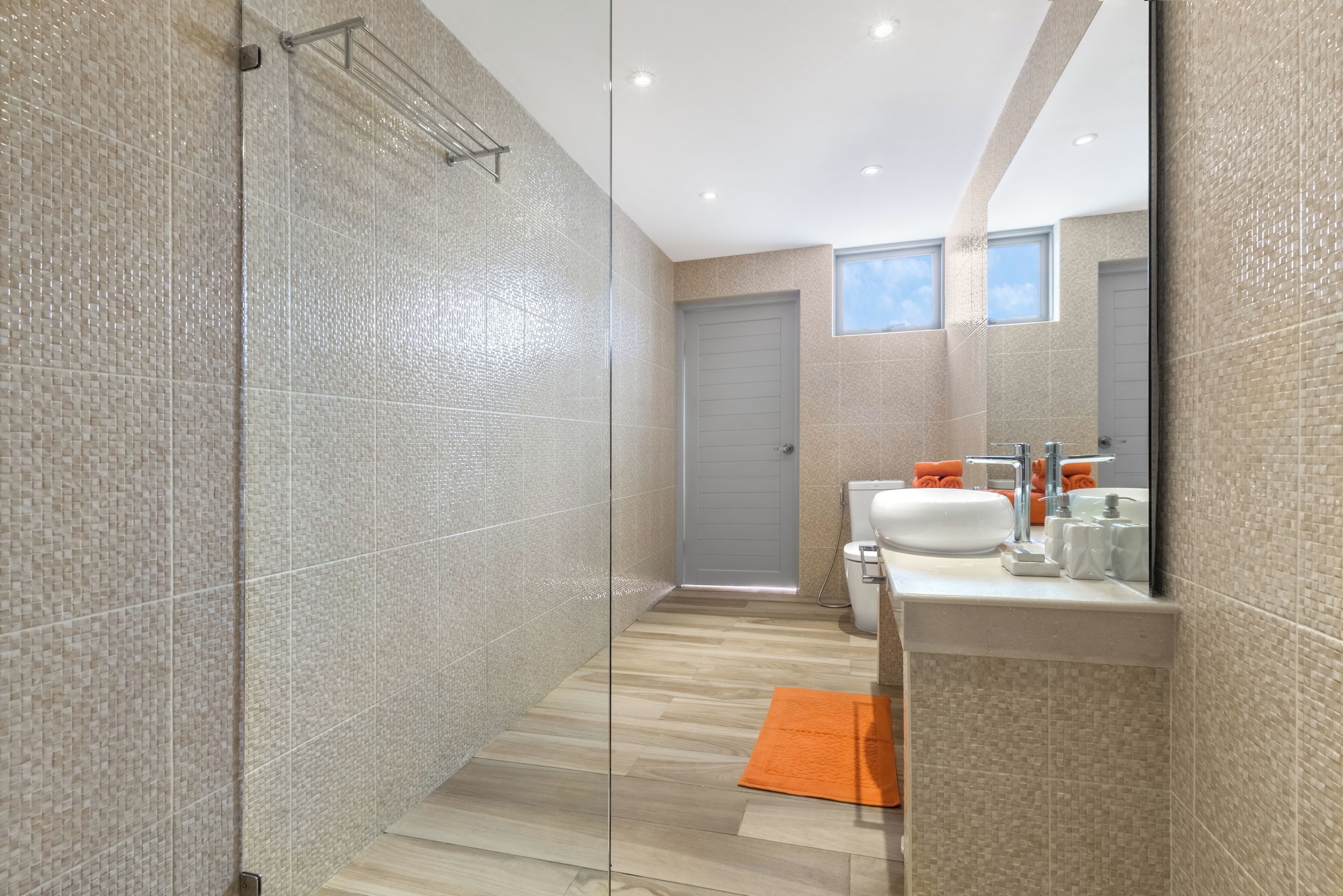 A modern bathroom with a glass shower enclosure, a sink with a mirror, and a wooden floor.