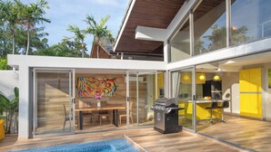 Una casa moderna con piscina, barbecue e zona pranzo con mobili gialli.