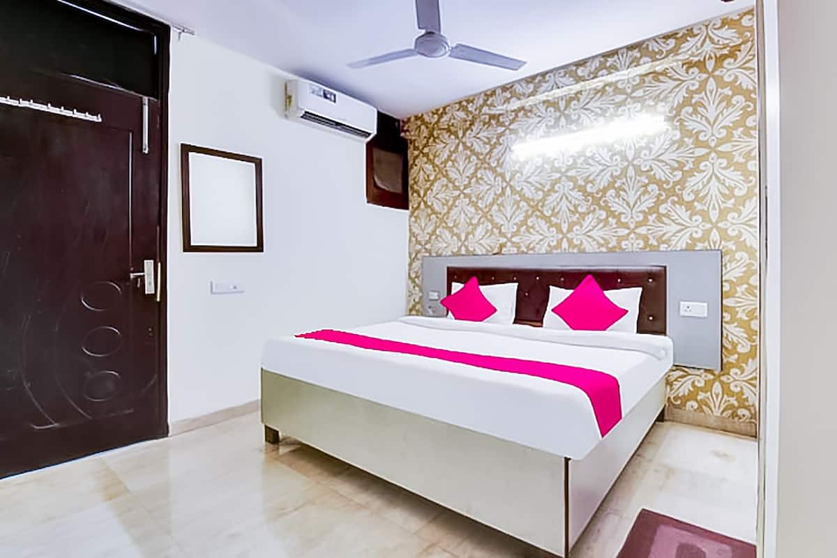 A bedroom with a bed, a ceiling fan, an air conditioning unit, a door, and patterned wallpaper.