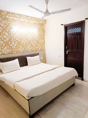 A bedroom with a bed, a ceiling fan, patterned wallpaper, and a door. - Roomshala 118 Hotel Acclaim 7 sky (New Delhi)