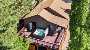 Vue aérienne d’un chalet doté d’un jacuzzi sur la terrasse, entouré d’arbres.