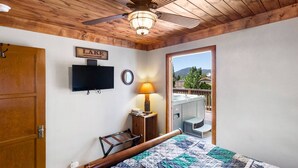 Une chambre avec un plafond en bois, une télévision, un lit avec une couette, une lampe et une vue sur un jacuzzi et des montagnes.